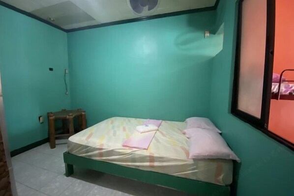 A small, single-bed room with teal walls, a wooden stool, and a window with a metal frame. - RedDoorz @ Classique Pan Oriental Hotel and Resort Batangas (Batangas Province)