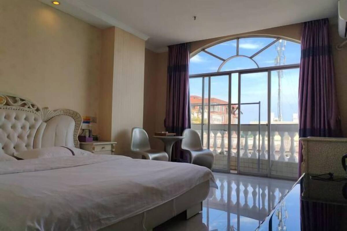Une chambre d’hôtel avec un grand lit, un balcon avec vue, une petite table et une chaise.