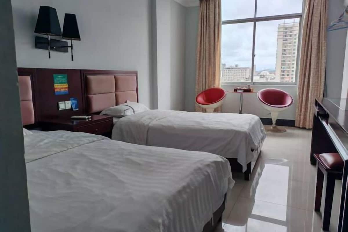 Une chambre d’hôtel avec deux lits, un bureau, une chaise, une fenêtre avec des rideaux et une vue sur des immeubles.