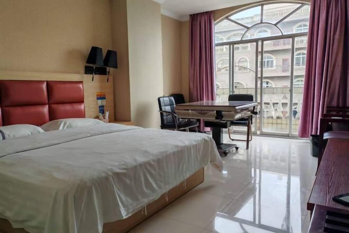 Une chambre d’hôtel avec un grand lit, un bureau avec une chaise, une télévision et une vue sur les immeubles, visible à travers une grande fenêtre.