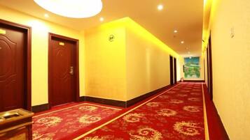 A hotel corridor with a red carpet, doors, and a ceiling light fixture.