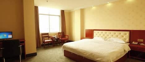 A hotel room with a large bed, a desk, a chair, and a TV.
