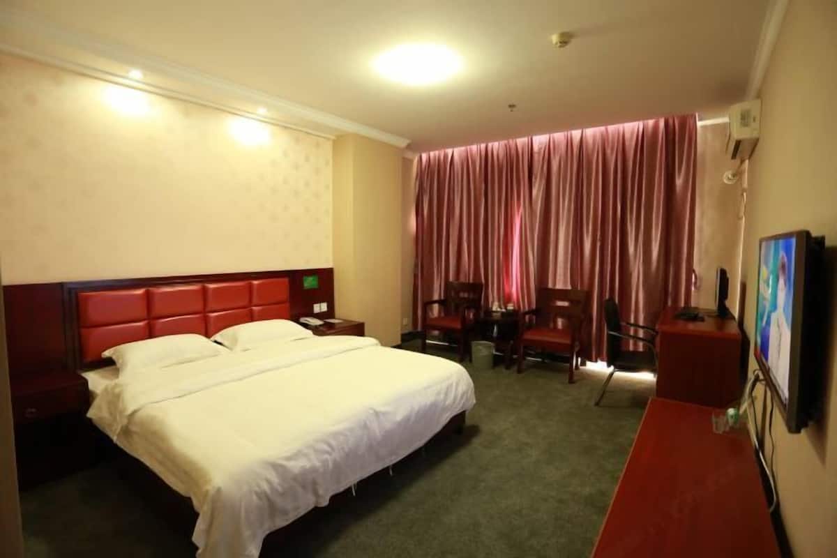 Une chambre d’hôtel avec un grand lit, un bureau, une chaise, une télévision et une fenêtre avec des rideaux.