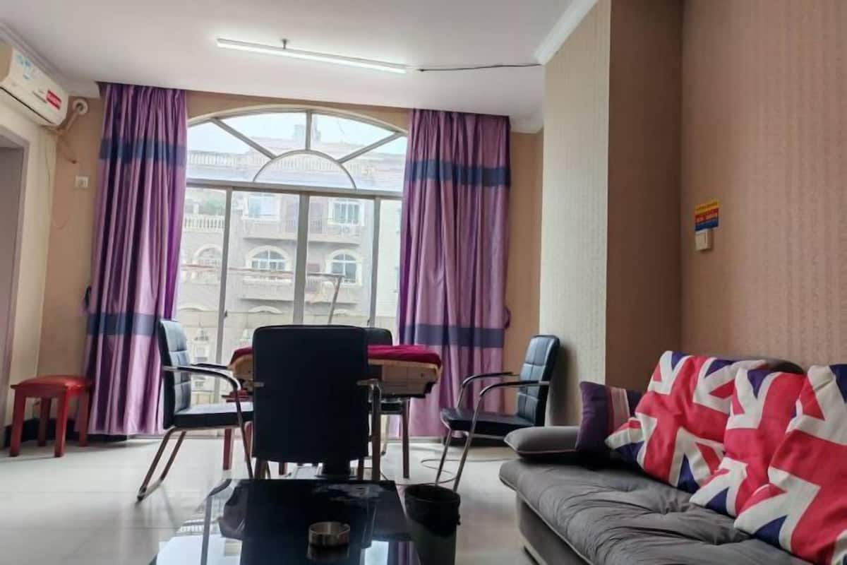Un salon avec un canapé, des fauteuils, une table et une fenêtre avec des rideaux.
