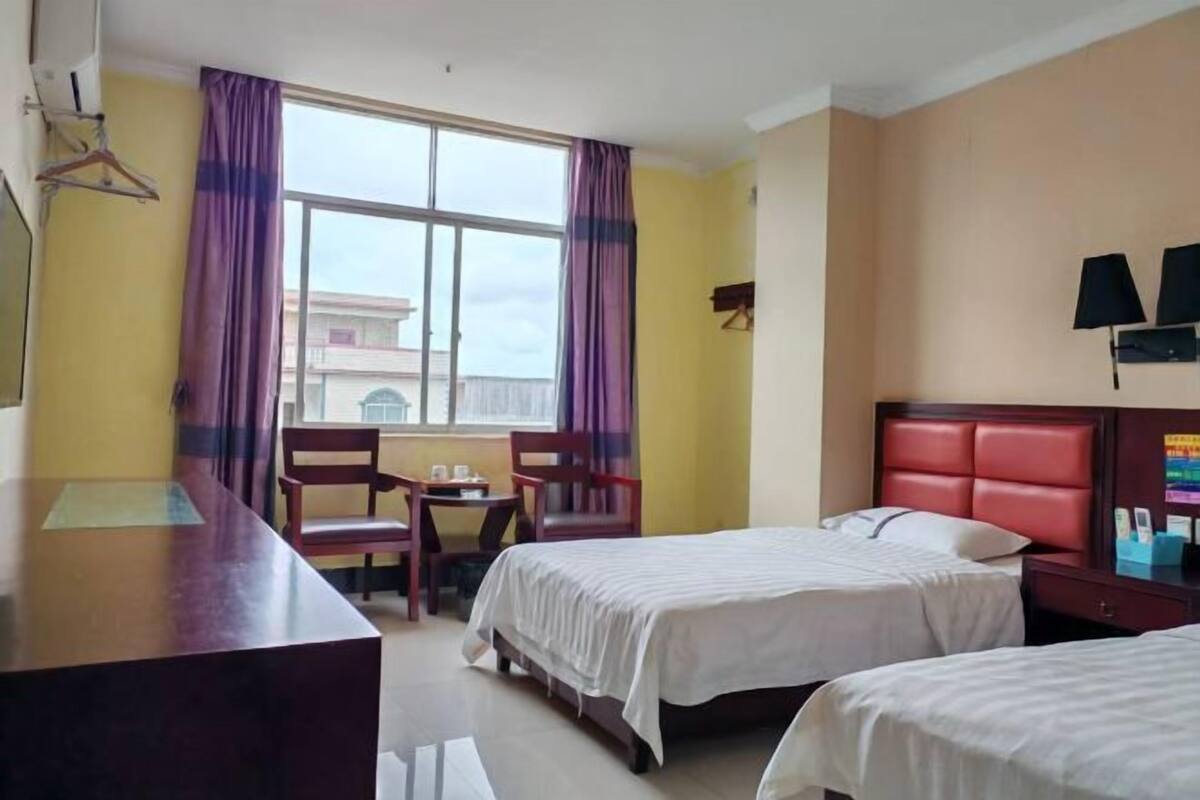 Une chambre d’hôtel avec deux lits, un bureau, des chaises, une fenêtre avec des rideaux et une lampe fixée au mur.