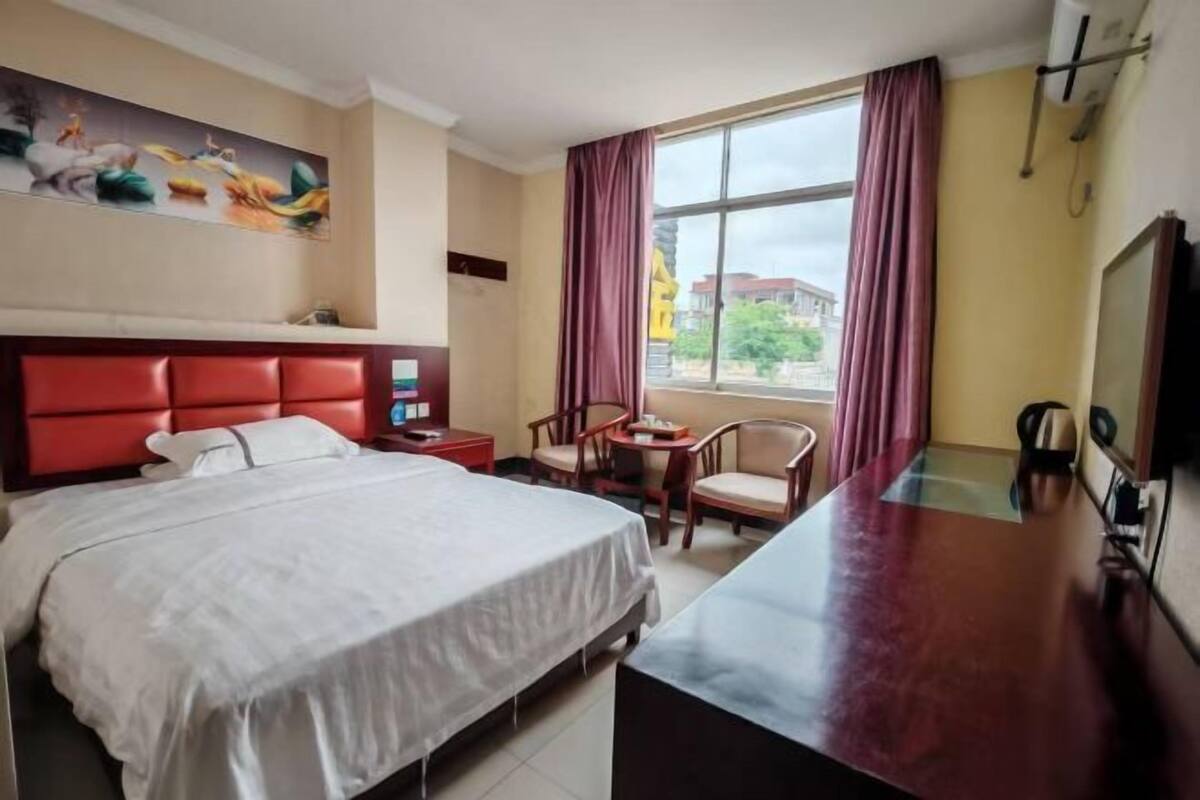 Une chambre d’hôtel avec un lit, un bureau, une chaise, une télévision et une fenêtre avec des rideaux.