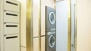A compact laundry room with a front-loading washer and dryer, a metal utility cabinet with numbered slots, and a glass door. - HanTing Hotel (Jiande Xin'an River Xindian) (Jiande)