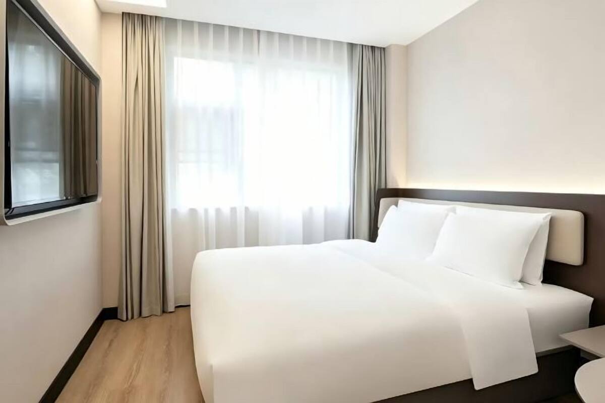 A hotel room with a large bed, a window with curtains, a bedside table, and a wall-mounted TV.
