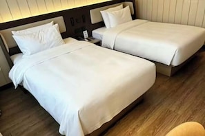 Hotellihuone, jossa on kaksi sänkyä, puulattia ja yöpöytä, jossa on lamppu.