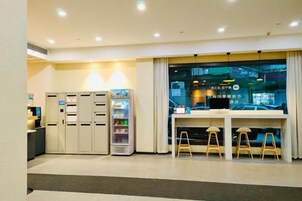 Un vestíbulo de hotel con una recepción, máquinas expendedoras y vistas a la ciudad a través de amplios ventanales.