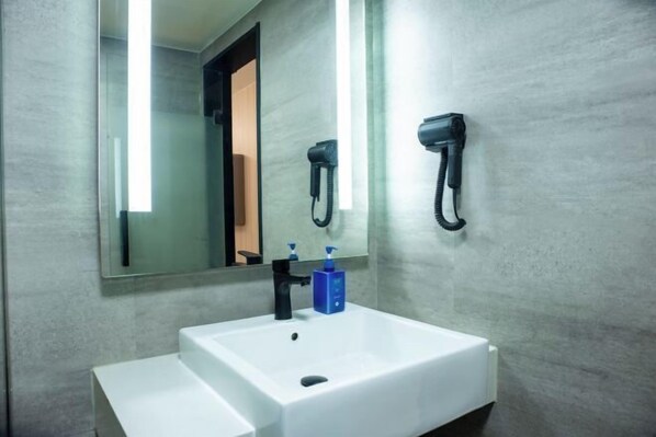 Un bagno con un lavandino bianco, uno specchio e un asciugacapelli montato a parete.