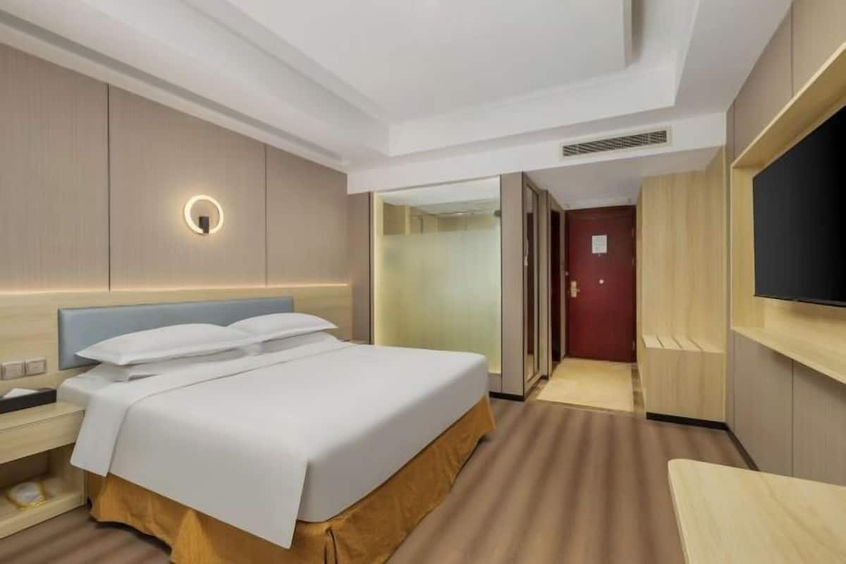 A hotel room with a bed, bedside table, TV, and a mirror.