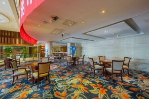 A hotel lobby with a patterned carpet, seating areas, and a large window overlooking a balcony.