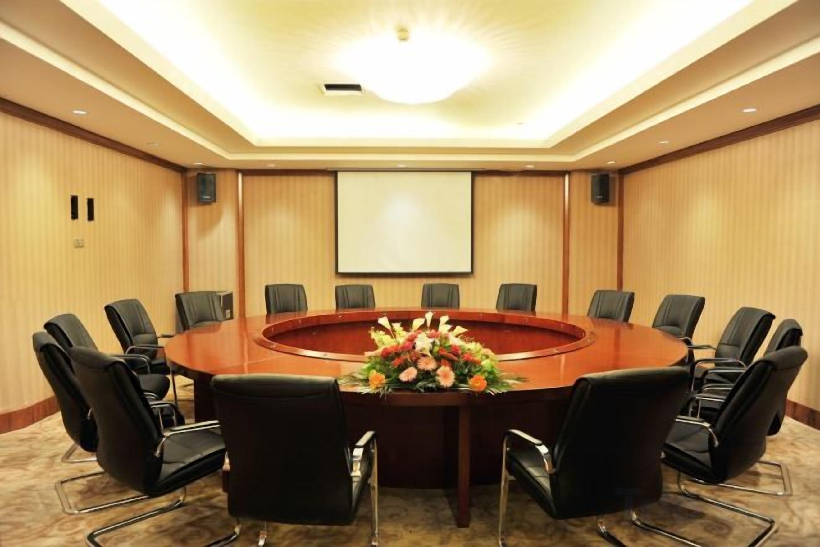 A conference room with a round table, black chairs, and a projector screen.