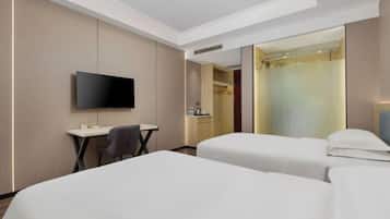 A hotel room with two beds, a desk, a chair, a TV, and a shower area.