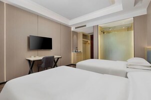 A hotel room with two beds, a desk, a chair, a TV, and a shower area.