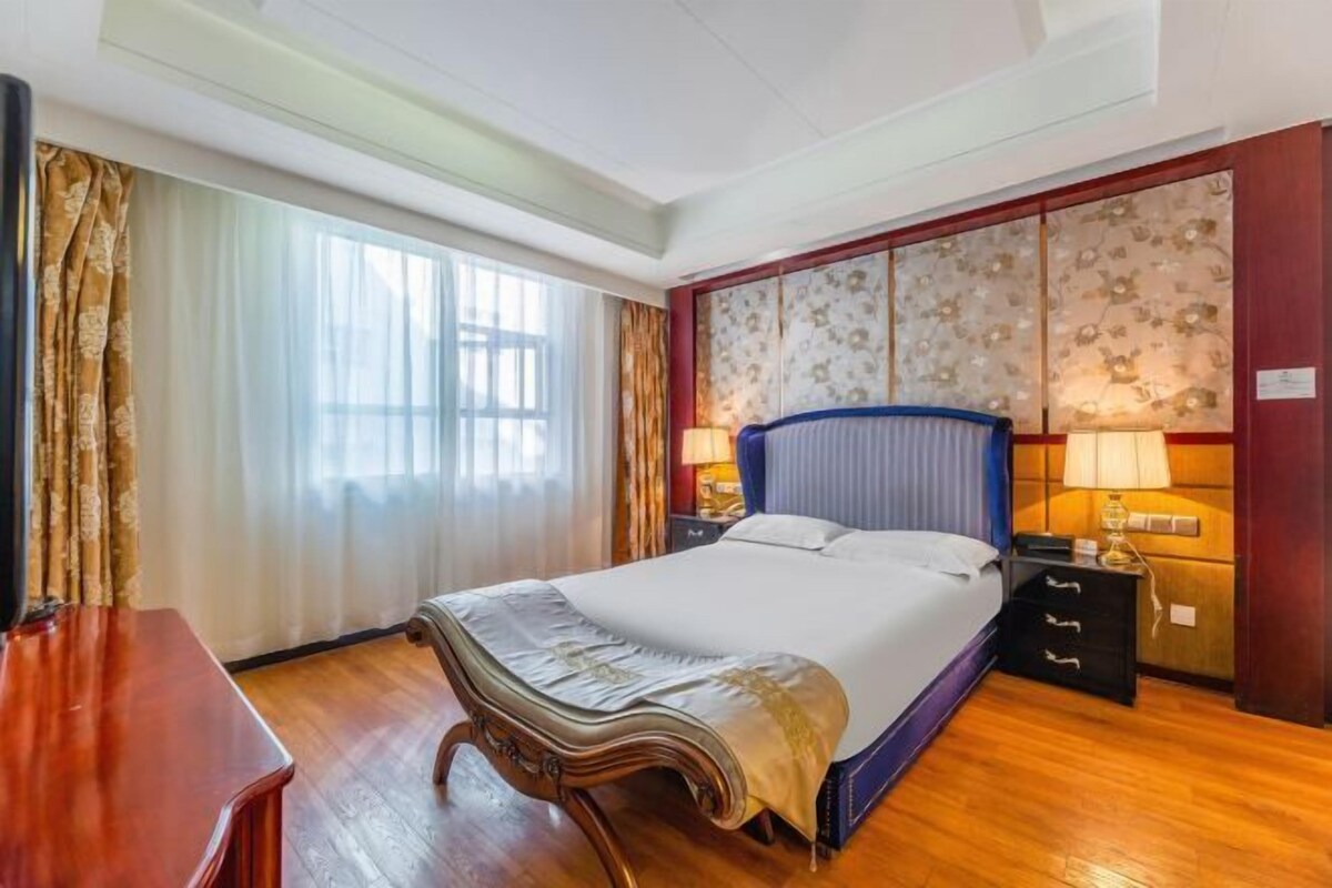 A hotel room with a large bed, wooden floor, a desk, and a nightstand with lamps.