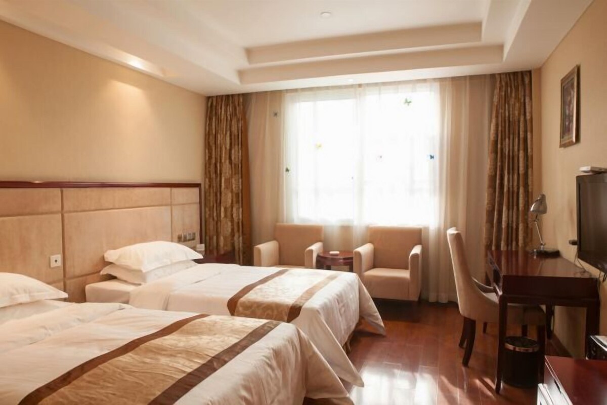 A hotel room with two beds, a desk, a chair, and a television.