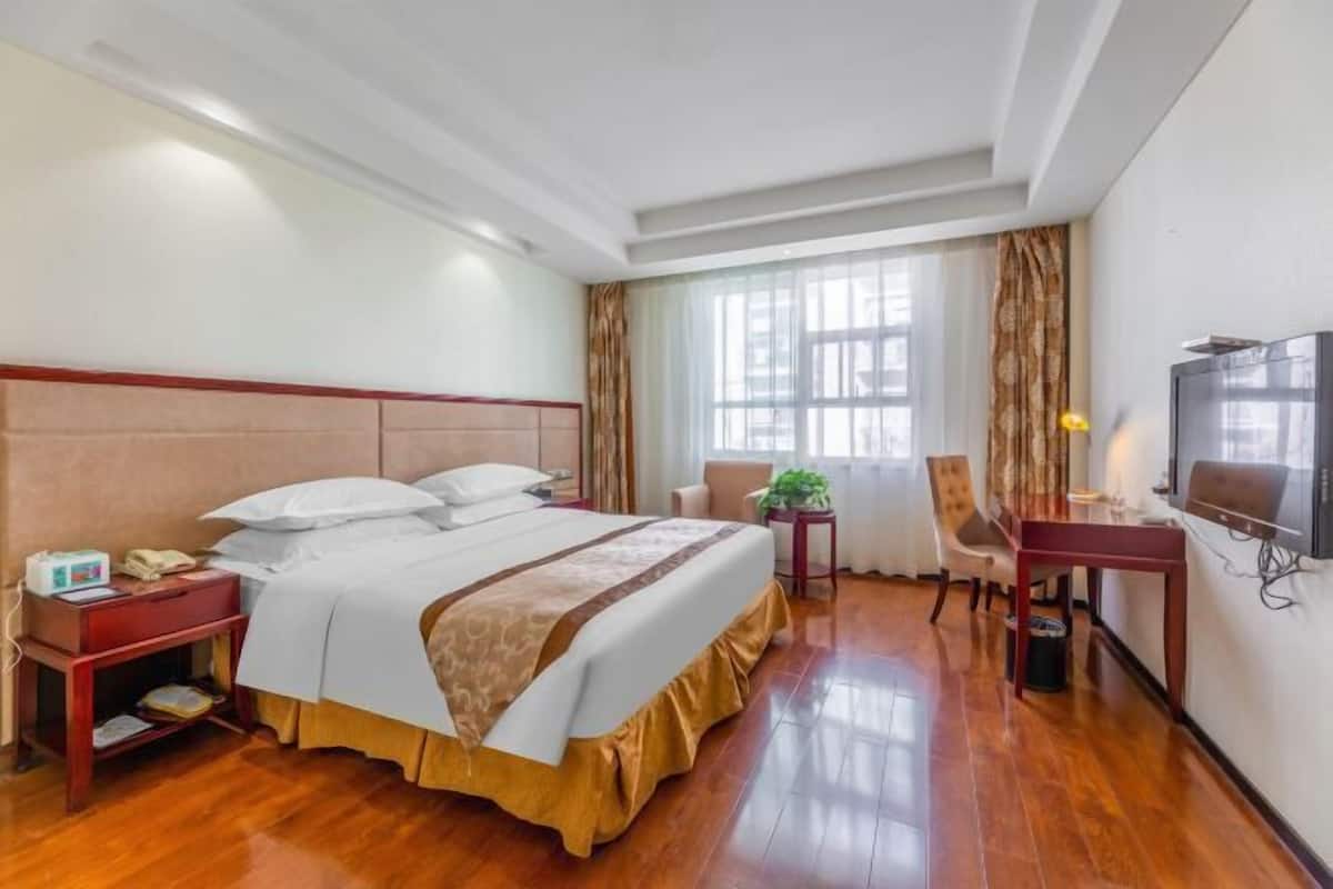 A hotel room with a large bed, a desk with a TV, a chair, and a window with curtains.