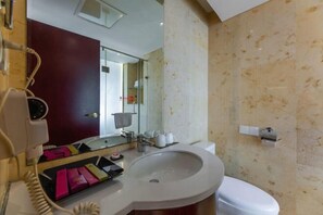 A bathroom with a white sink, a toilet, a mirror, and a hairdryer on the counter.