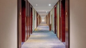 A hotel corridor with multiple doors on each side, a carpeted floor, and recessed lighting. - Halcyon Hotel & Resort (Yingtan)