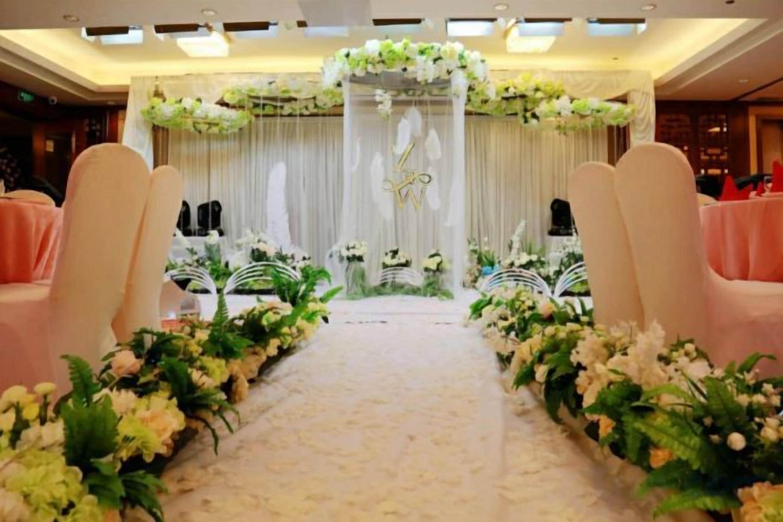 A stage with a floral archway, a carpeted aisle, and pink chairs on either side.