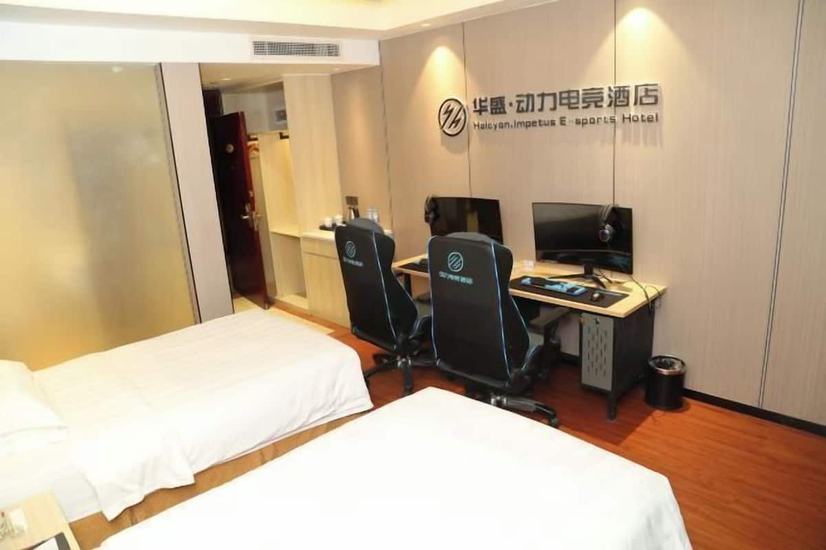 A hotel room with two single beds, a desk with two monitors, and a chair.