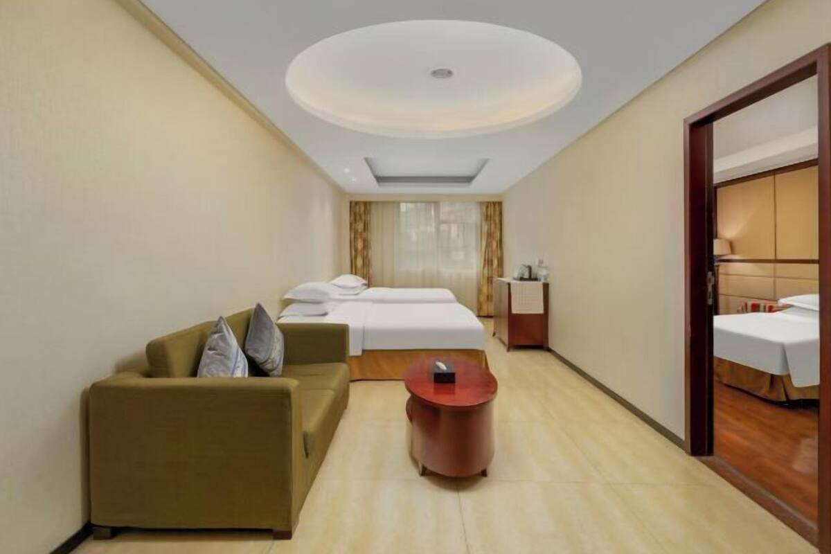 A hotel room with a bed, a sofa, a small table, and a mirror.