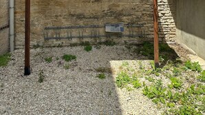 A courtyard with a pergola, red flowers, a stone wall, and a gravel ground.