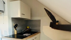 A compact kitchen with a black stove, white cabinets, a small trash bin, and a wooden floor.