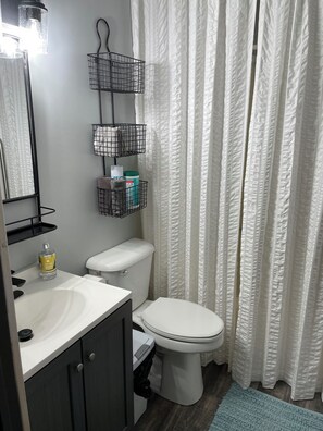 A bathroom with a white toilet, a sink with a mirror, and two black wire baskets on the wall.