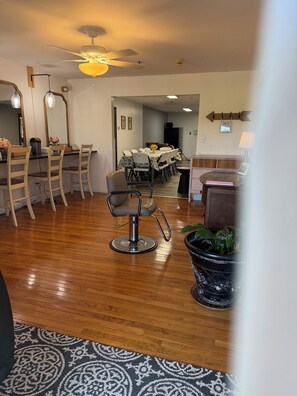 A room with a dining table, chairs, a ceiling fan, a potted plant, and a desk with a lamp.