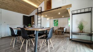 A modern dining area with a wooden table and chairs, a loft-style ceiling, and a view of a green outdoor area. - Lovely home in Sonlez with sauna (Sonlez)