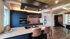 A modern kitchen with dark cabinetry, a central island with bar stools, and a built-in oven. - Lovely home in Sonlez with sauna (Sonlez)