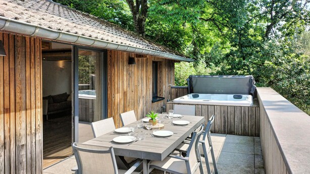 An outdoor dining area with a table set for two, surrounded by wooden walls and a hot tub. - Lovely home in Sonlez with sauna (Sonlez)