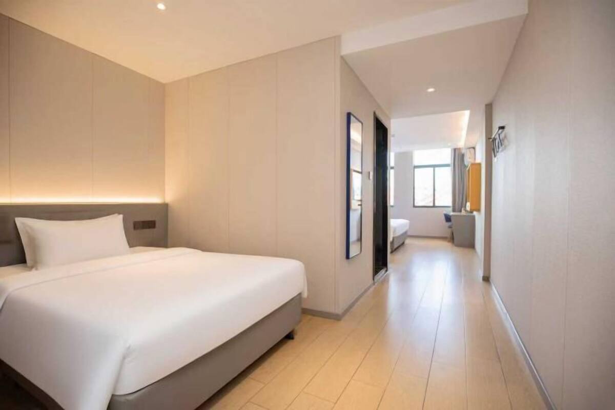 A hotel room with a large bed, a bedside table, and a view of the hallway.