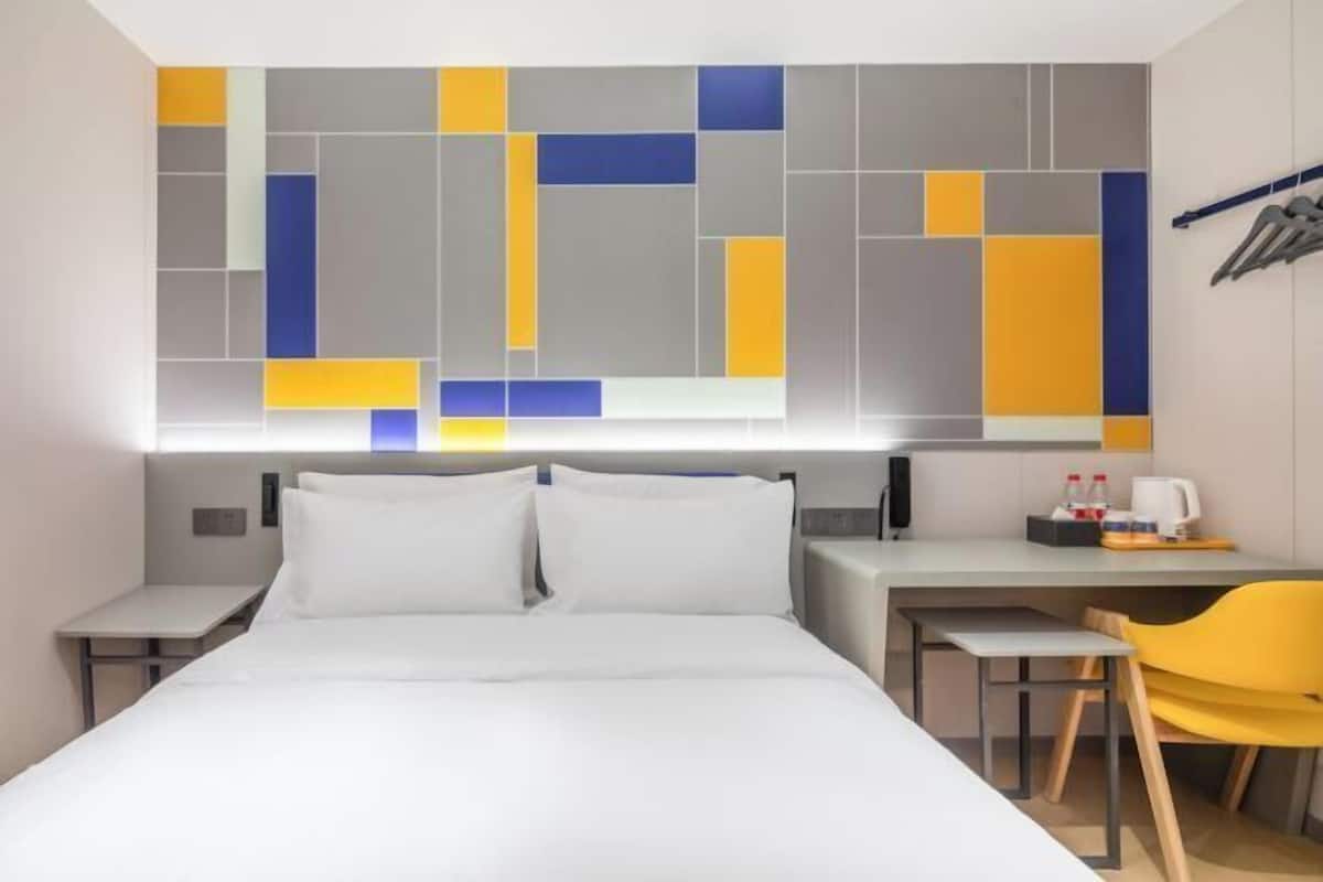 A hotel room with a bed, a desk, a chair, and a wall art piece.