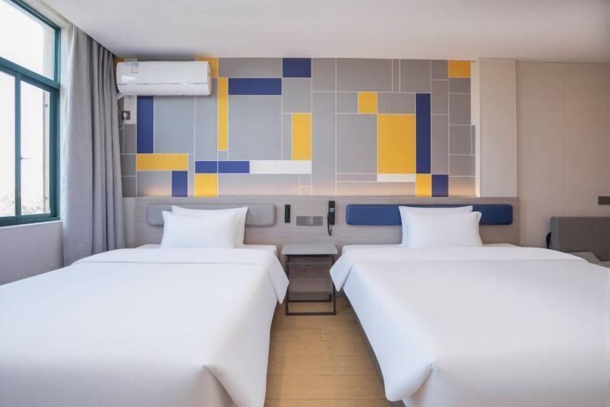 A hotel room with two beds, a modern wall design, and a window with curtains.