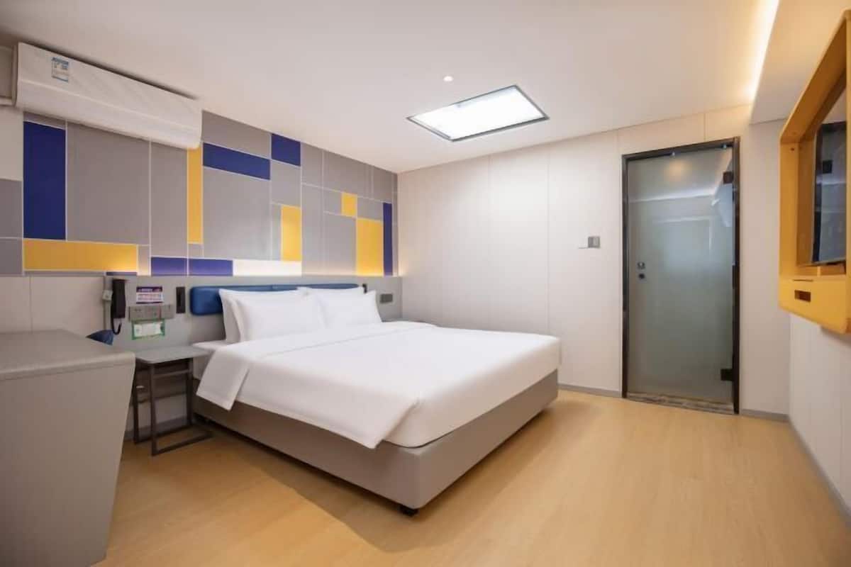 A modern hotel room with a bed, bedside table, and a glass door.