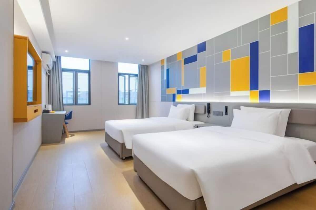 A hotel room with two beds, a desk, and a large window.
