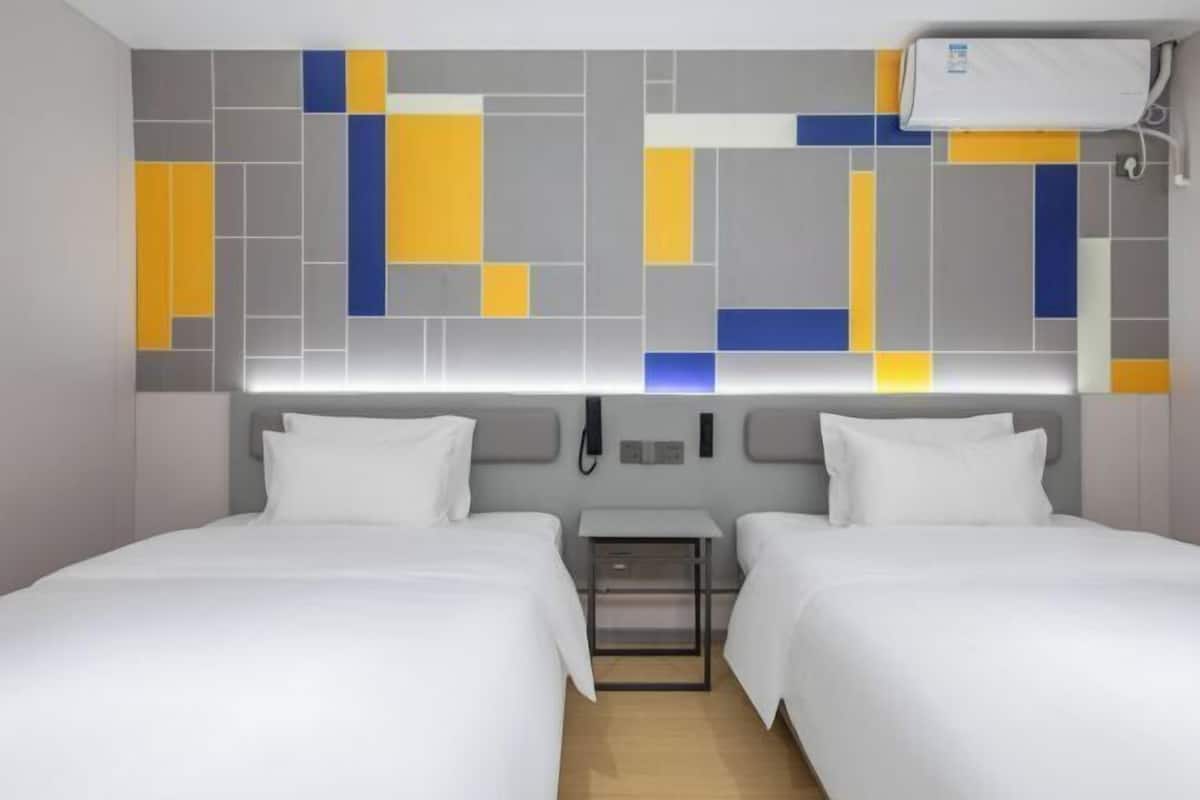 A hotel room with two beds, a bedside table, a wall-mounted phone, and a ceiling air conditioner.