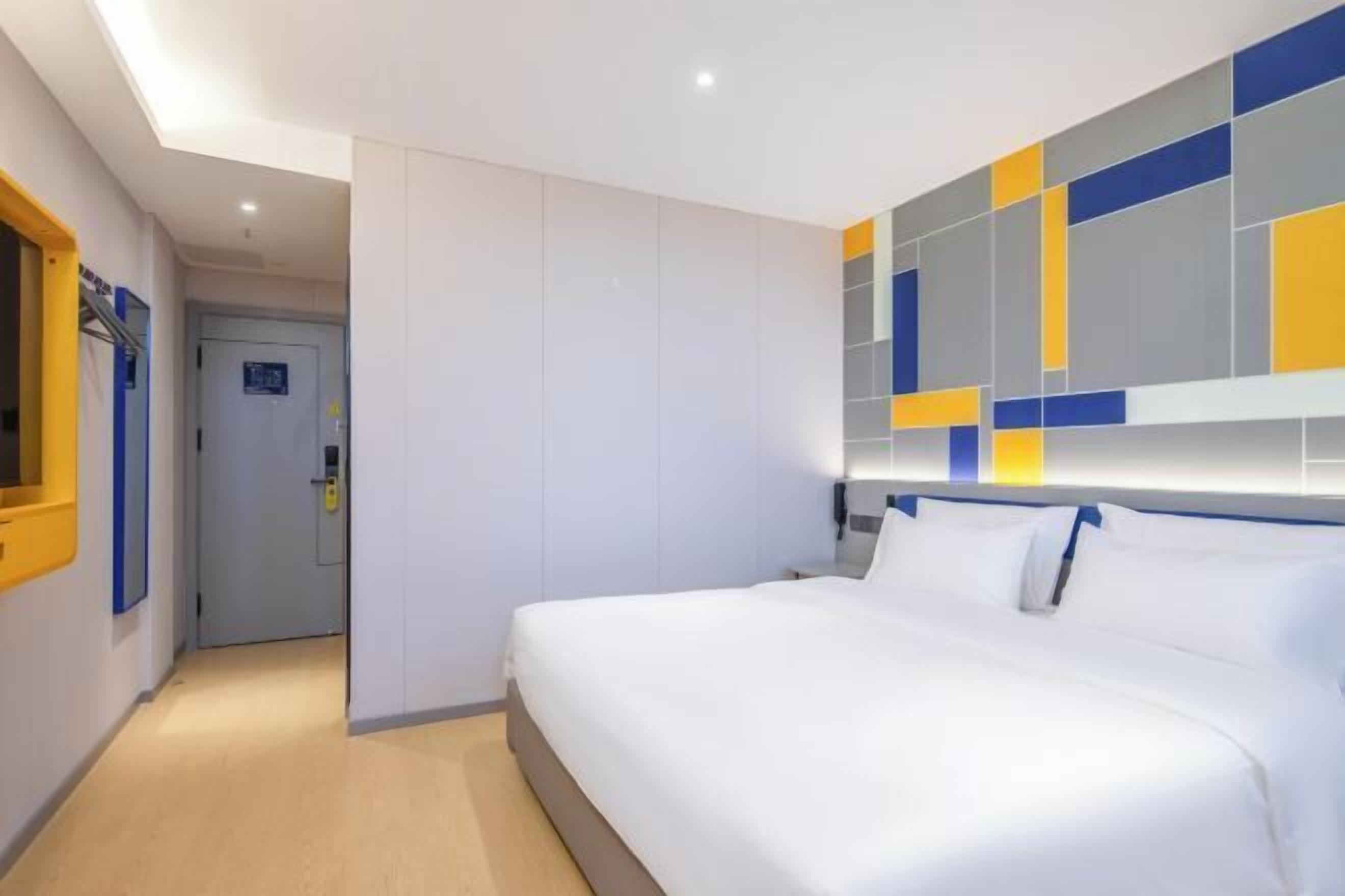A hotel room with a large bed, a wall with geometric patterns, and a door in the background.