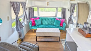 Un interior de caravana acogedor con un sofá color turquesa, una mesa de centro de madera y una pequeña cocina americana en un lateral.