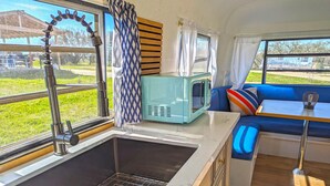 Una kitchenette compacta con un lavamanos, un microondas y una ventana con cortinas.