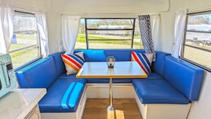 Un interior acogedor con asientos azules, una mesa pequeña y un ventanal con cortinas.