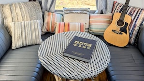 Ein gemütliches Interieur mit einer Couch, einem kleinen runden Tisch, einer Gitarre und einem Buch mit dem Titel 'LEDZEFFELN' von LED ZERFELIN.