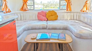 A cozy seating area with a cushioned bench, a small wooden table with books, and orange curtains.