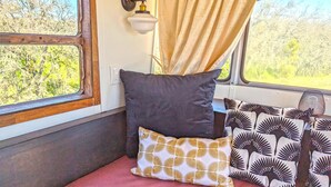 Ein gemütliches Interieur mit Fenster, einer Wandleuchte und einem Bett mit gemusterten Kissen.