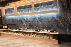 A hotel reception area with a marble wall, a reception desk, and a display of various items on shelves. - Gangxing Hotel (Zhuji)