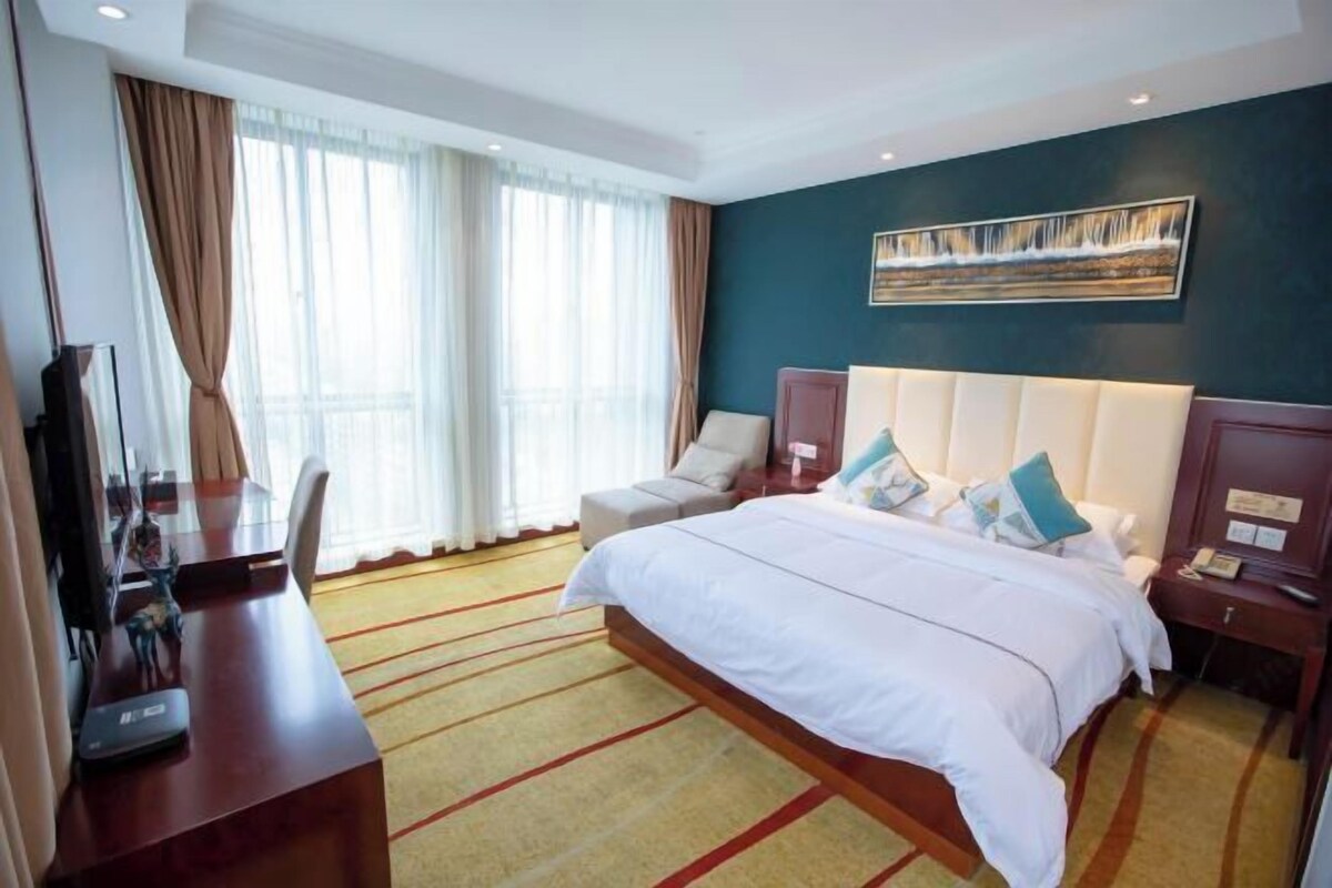 A hotel room with a large bed, a desk with a computer, a chair, and a painting on the wall.